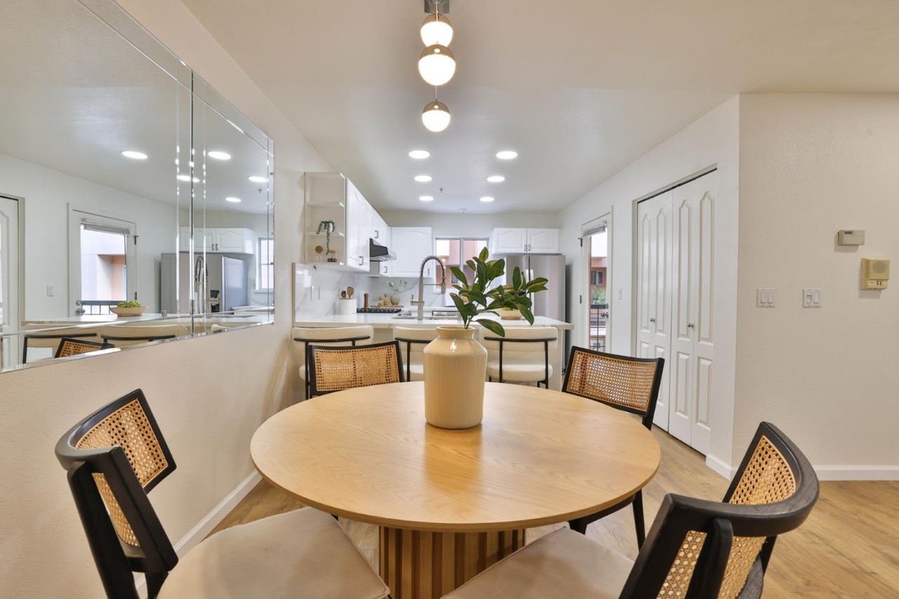 Dining nook with a round wood table, cane-back black chairs, three pendant globes overhead, and the white kitchen visible to the right