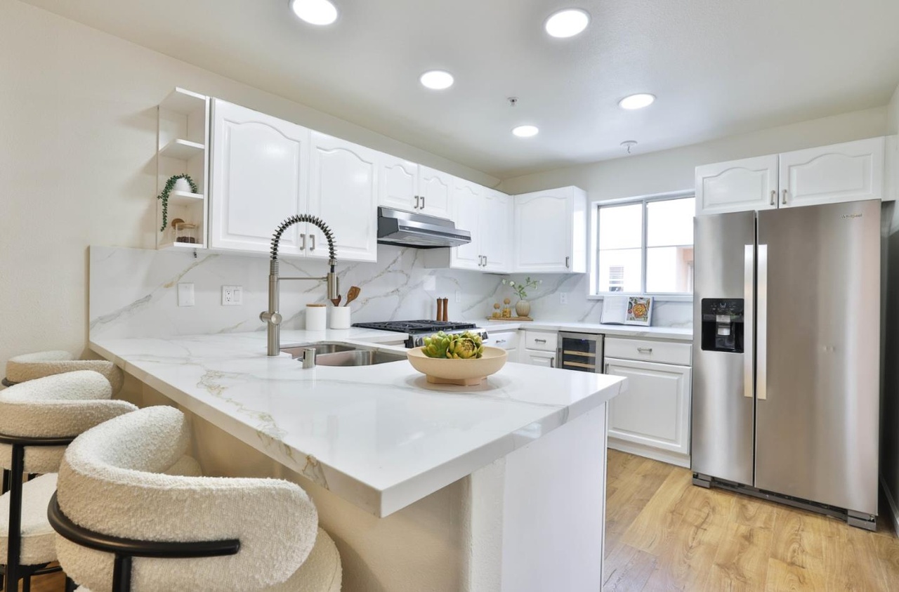 Kitchen with a marble-veined quartz peninsula, white cabinetry, stainless steel appliances, a gas range, and a side entry to a small balcony