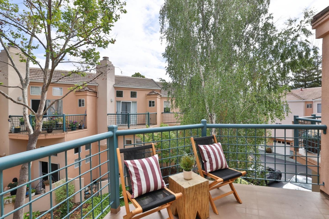 Upstairs balcony with a metal wire railing, two red-and-cream striped canvas sling chairs and a small wood side table, framed by a birch tree