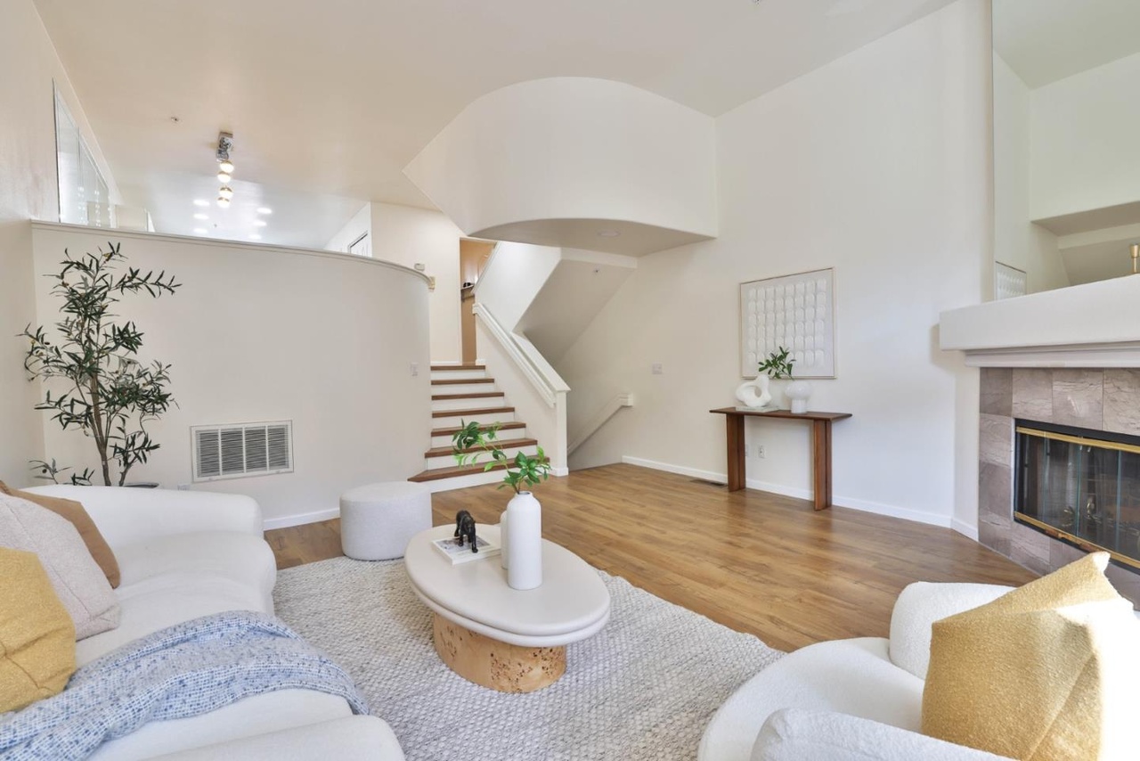 The great room at 970 Asilomar Terrace Unit 3, with sixteen-foot ceilings, a mirrored chimney breast, a tile-front fireplace, a curved partial wall, and a raised upper landing above the stair.